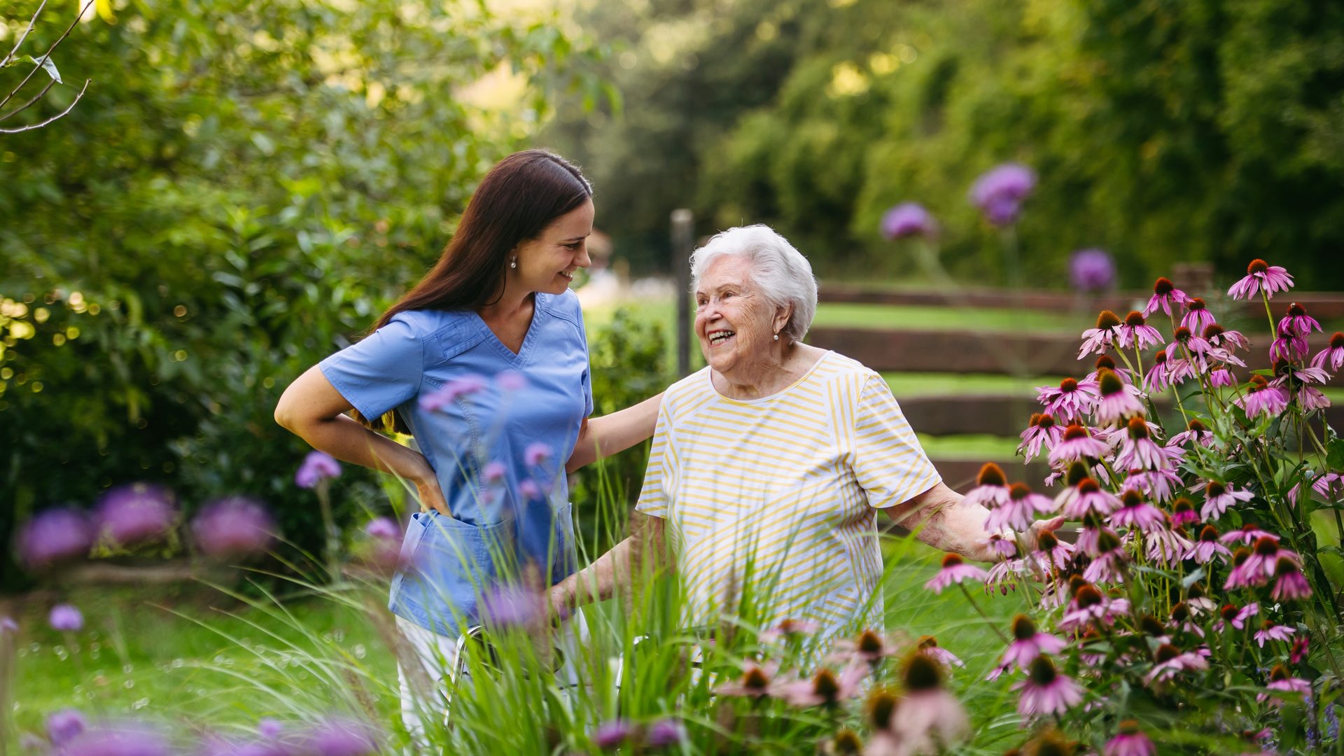A carer and an older woman enjoying a garden together